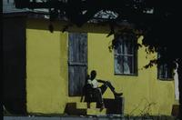 Man seated by yellow house