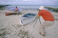 Man on beach in pink shirt with boats and photographers