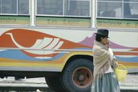 A woman in a hat stands in front of a colourful bus