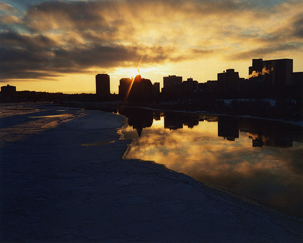 Silhouette of downtown Saskatoon, the sunset reflecting in the river.