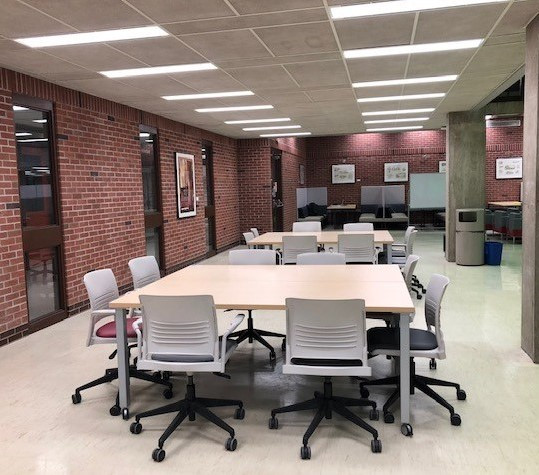 Bookable meeting space in the University Library Learning Commons in the College of Engineering. There are two square tables with two rolling chairs on each side situated next to a brick wall with concrete pillars on the opposite side.
